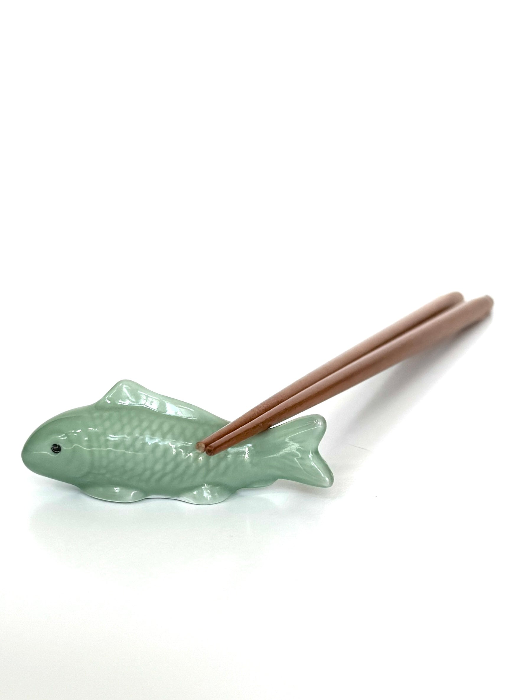 Green fish-shaped chopstick rest with wooden chopsticks on a white background